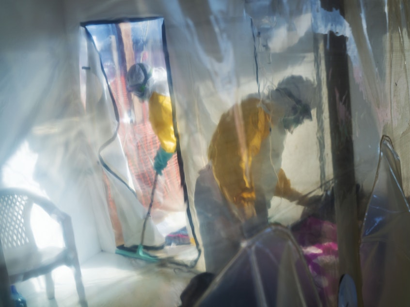 caption: Health workers in protective suits tend to an Ebola victim kept in an isolation cube in Beni in the Democratic Republic of Congo.