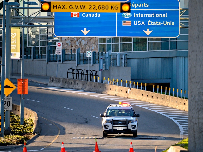 caption: Canada plans to impose a new vaccine mandate on passengers and workers in the federally regulated air, rail and cruise ship sectors. Here, a police car is seen behind traffic cones near Vancouver International Airport in May.