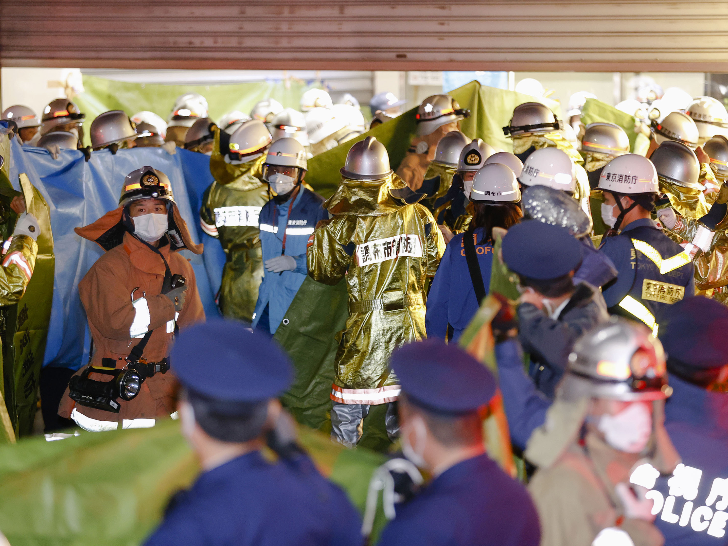 caption: Emergency workers and police officers are seen at a train station in Tokyo on Sunday, after a man brandishing a knife on a commuter train stabbed several passengers before starting a fire.