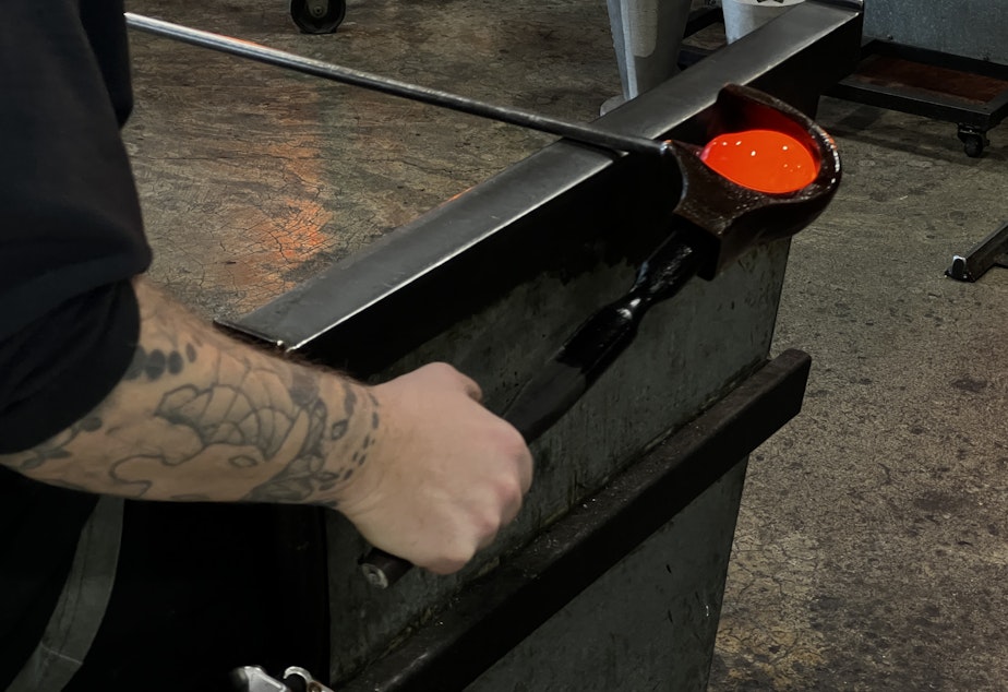 caption: Here, a glassblower fashions glass into a sphere. This particular piece will become a glass pumpkin, a classic piece from the glassblowing studio. 