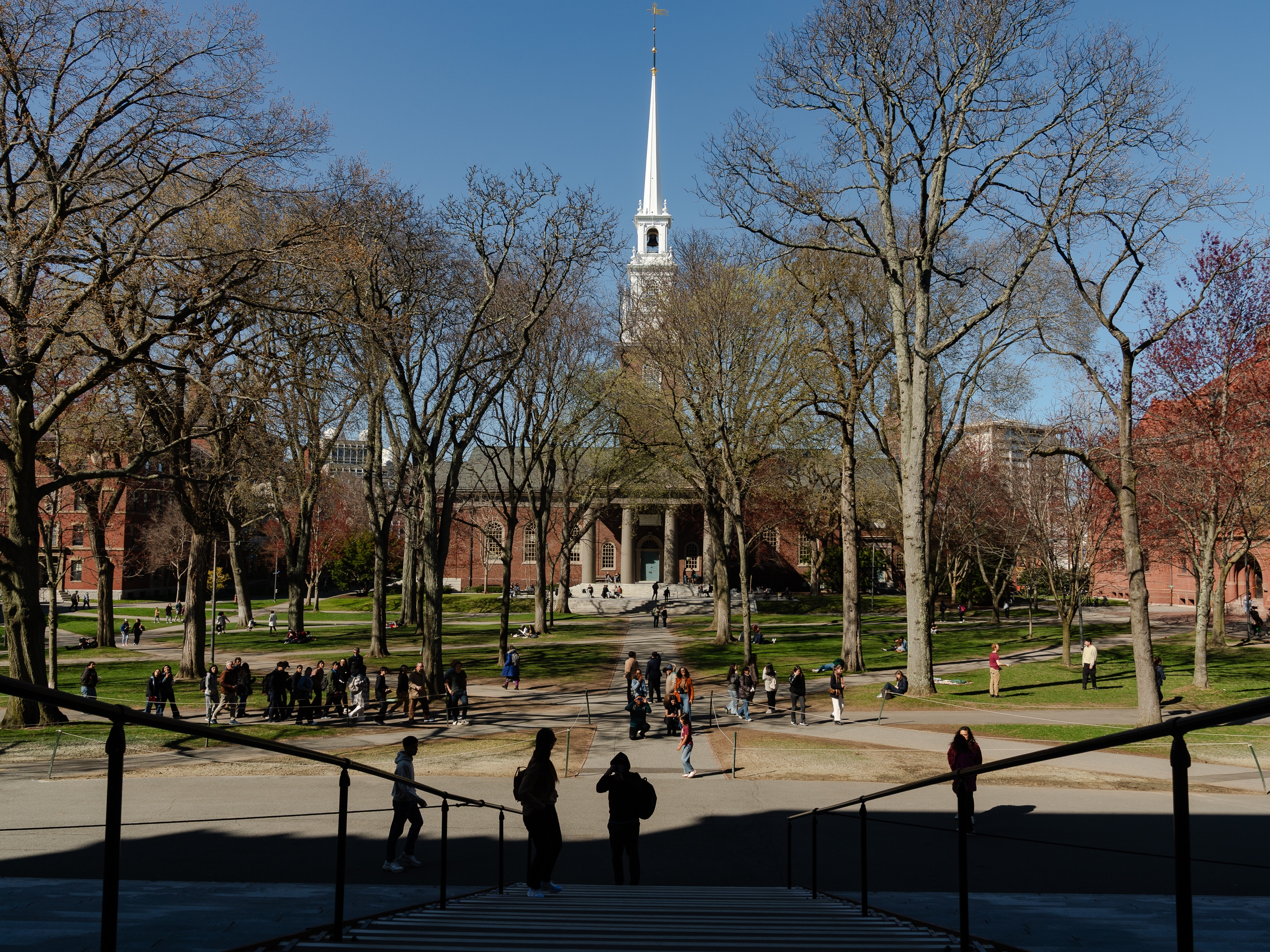 caption: People cross Harvard Yard at Harvard University on April 17, in Cambridge, Mass.