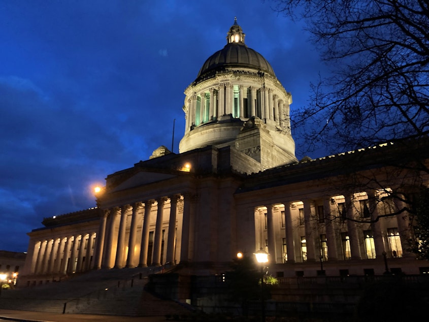 caption: The Washington state Capitol is lit up on a cloudy evening in Olympia.