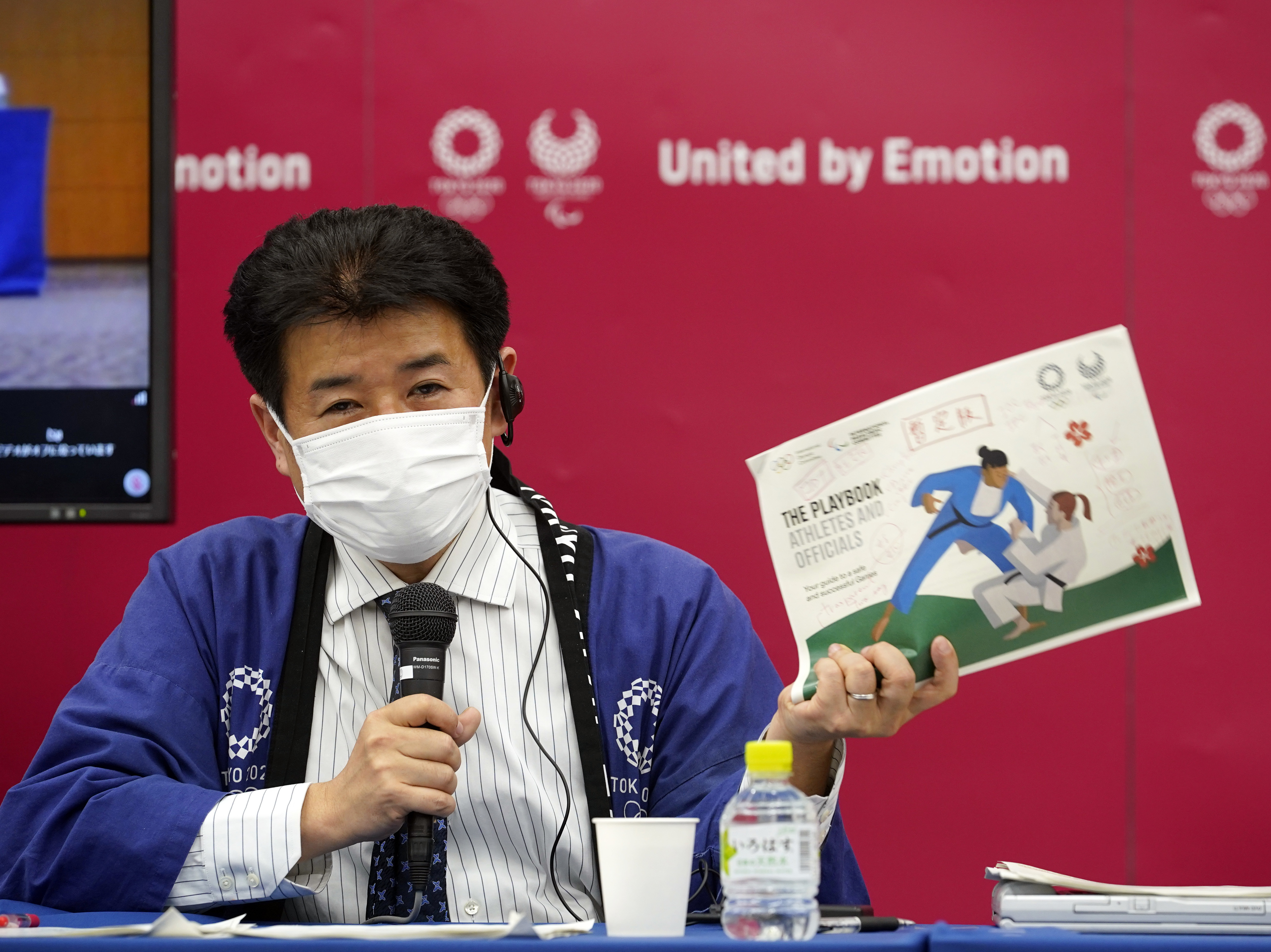 caption: Tokyo 2020 Games Delivery Officer Hidemasa Nakamura holds a sample of an updated version of the Tokyo 2020 Playbook during a news briefing on Wednesday.