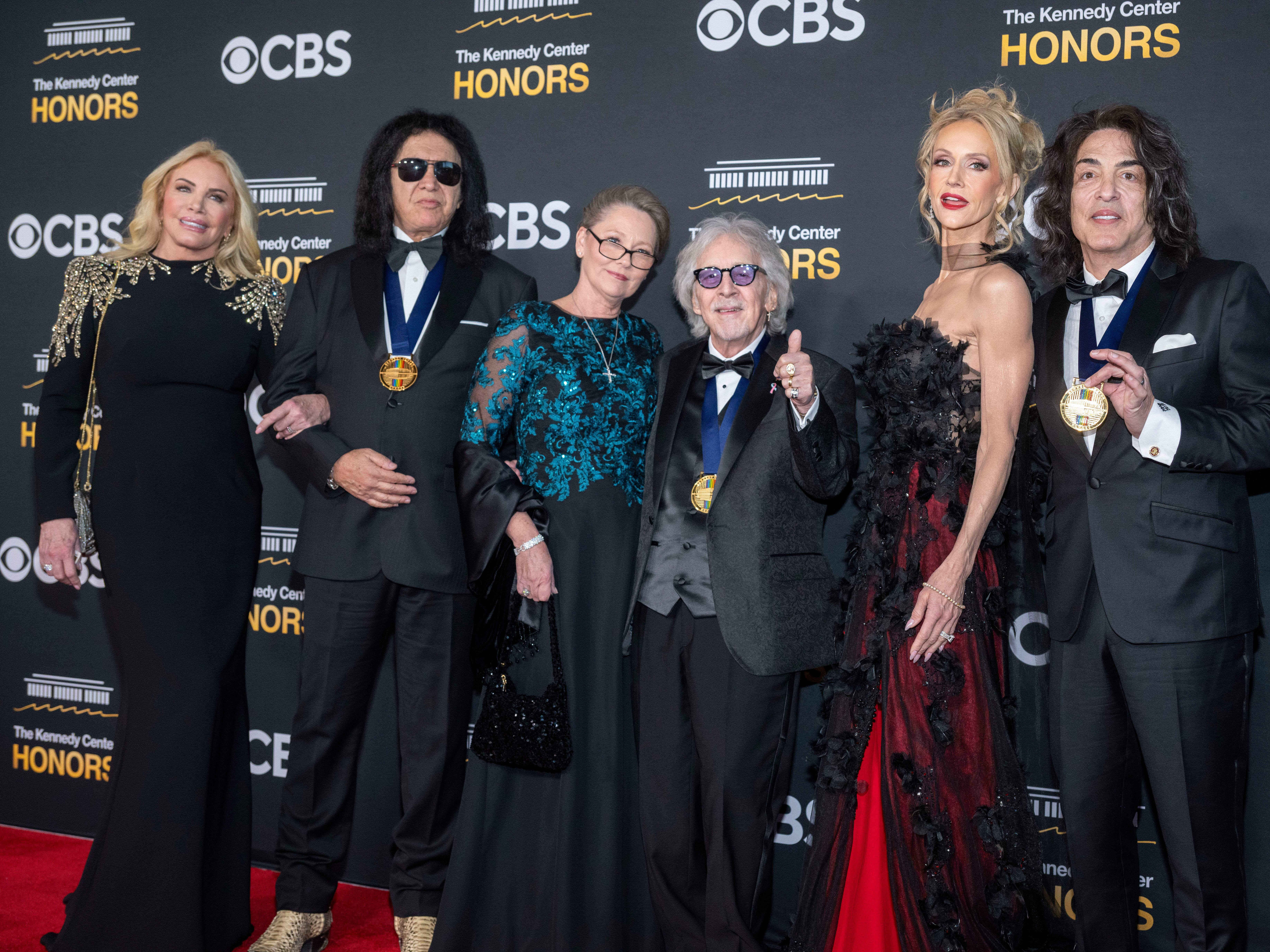 caption: From left, Shannon Tweed Simmons, 2025 Kennedy Center Honoree and member of rock band KISS Gene Simmons, Gigi Criss, 2025 Kennedy Center Honoree and member of rock band KISS Peter Criss, Erin Stanley and 2025 Kennedy Center Honoree and member of rock band KISS Paul Stanley pose on the red carpet for the 48th Kennedy Center Honors at the Kennedy Center for the Performing Arts.