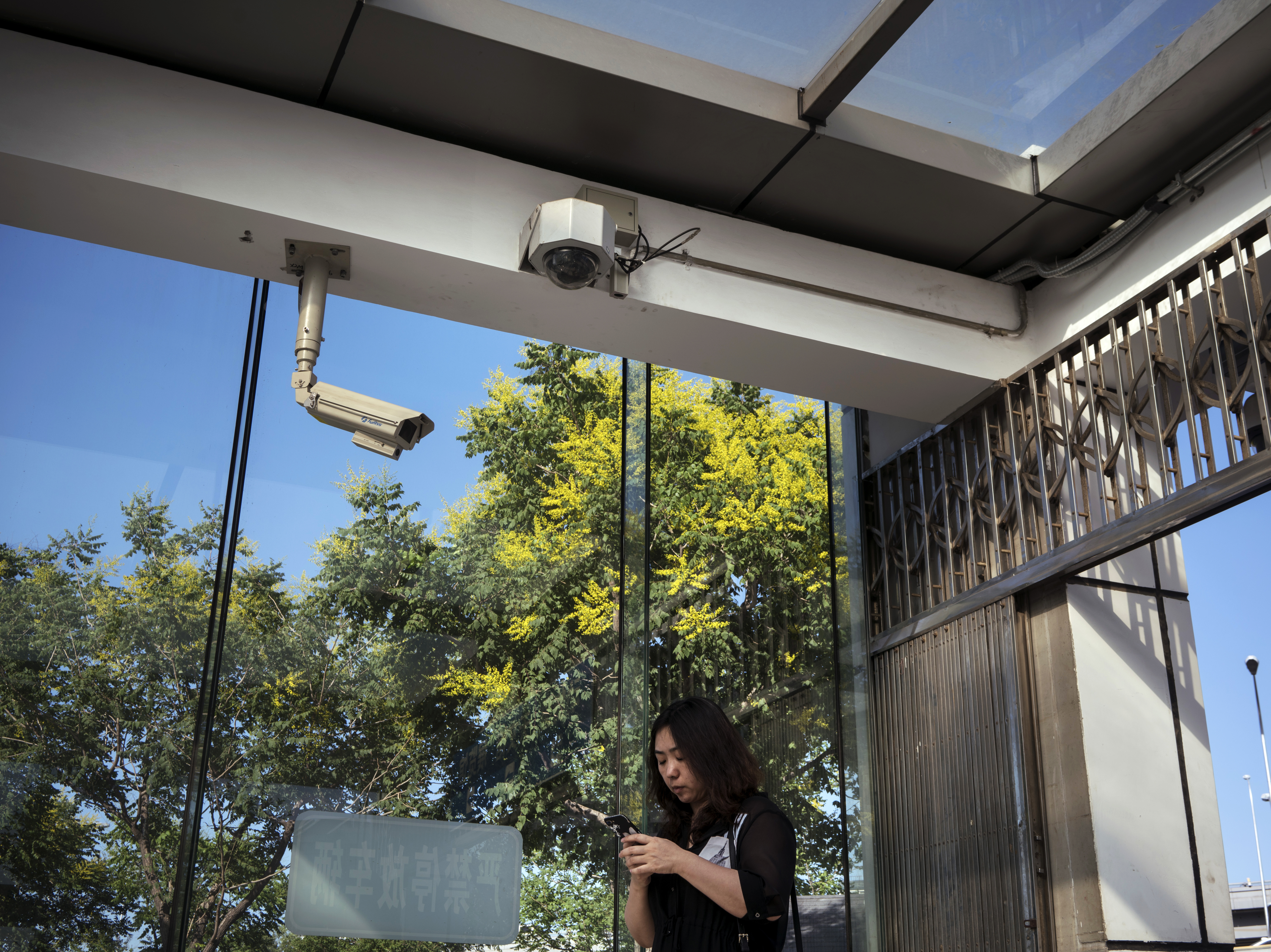 caption: A pedestrian uses a smartphone while standing under surveillance cameras in Beijing last May.