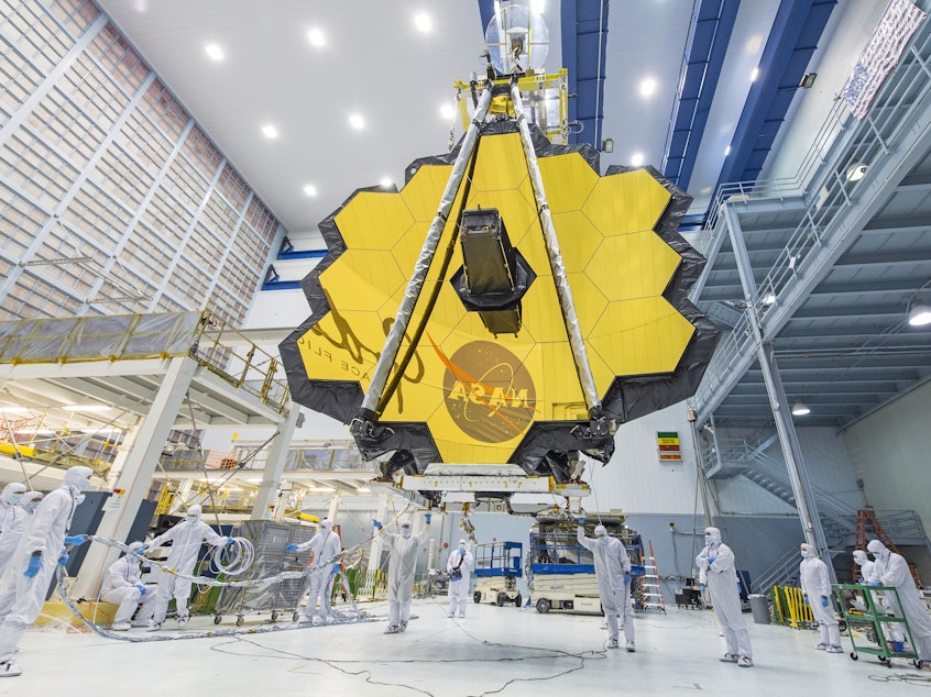 caption: In 2017, technicians lift the mirror assembly of the James Webb Space Telescope using a crane inside a clean room at NASA's Goddard Space Flight Center in Greenbelt, Md.