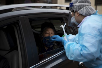 caption: Registered nurse Tina Nguyen administers a Covid-19 test on Friday, November 20, 2020, at the International Community Health Services drive thru testing site on 8th Avenue South in Seattle's International District. 