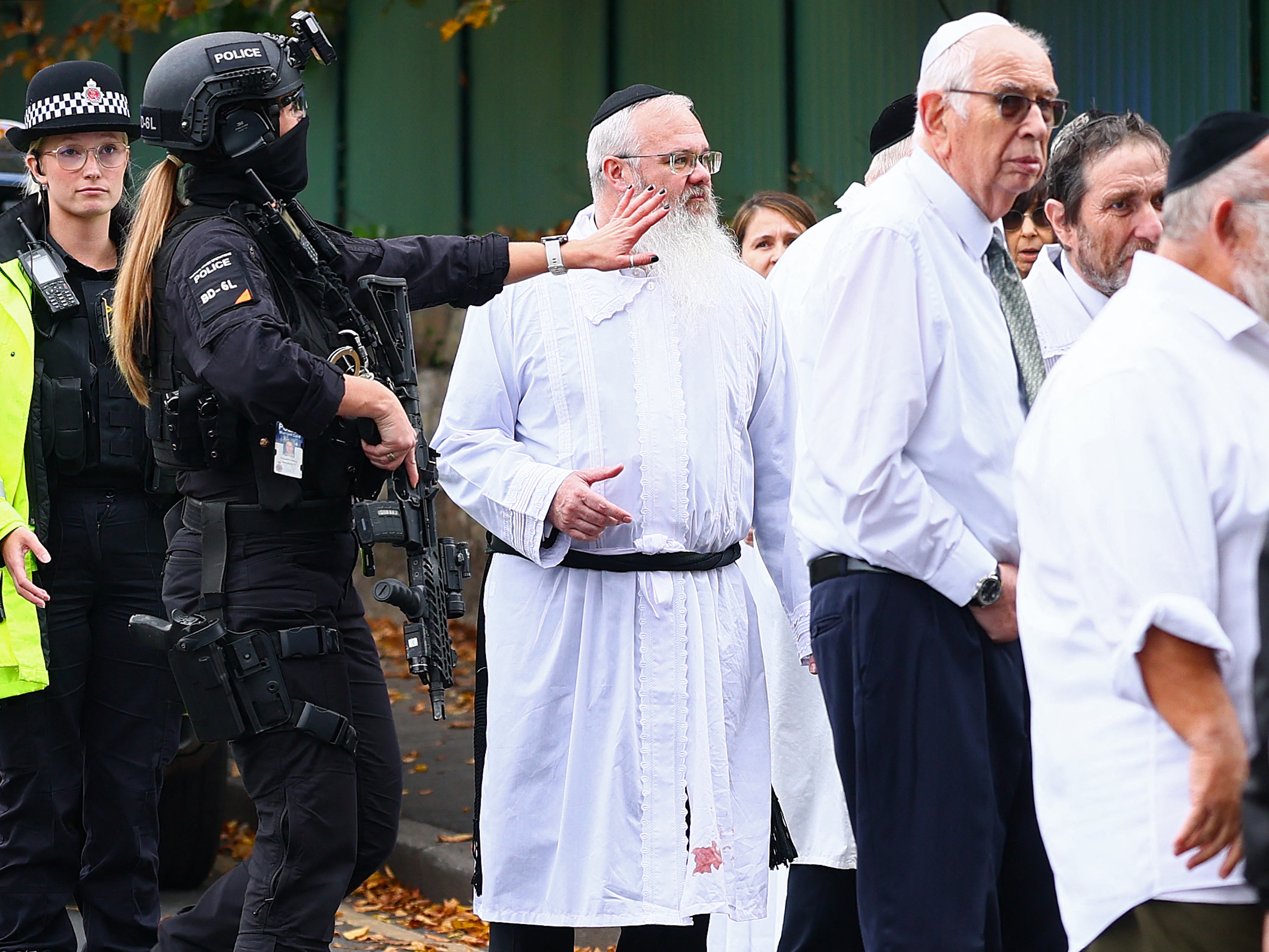 caption: Rabbi Daniel Walker (third from left) stands among armed police officers as they talk with members of the Jewish community outside Heaton Park Hebrew Congregation synagogue in Crumpsall, north Manchester, following an attack at the synagogue on Thursday.