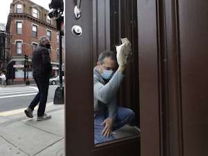 caption: Manager Mike Bonavita wears a protective mask as he cleans windows at the Quattro Italian restaurant in Boston on May 12 during the coronavirus pandemic. This month, Massachusetts' governor declared wearing masks mandatory.