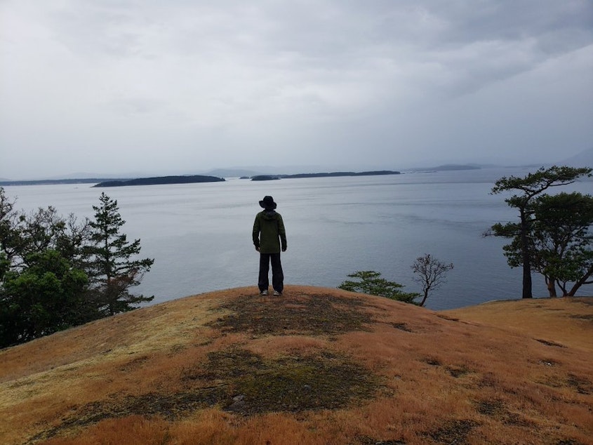 caption: KUOW's John Ryan looks out at Canada's Moresby and Saltspring islands from Turn Point, Stuart Island, Washington, in 2019. Washington's deepest spot is hidden beneath the waves in between.
