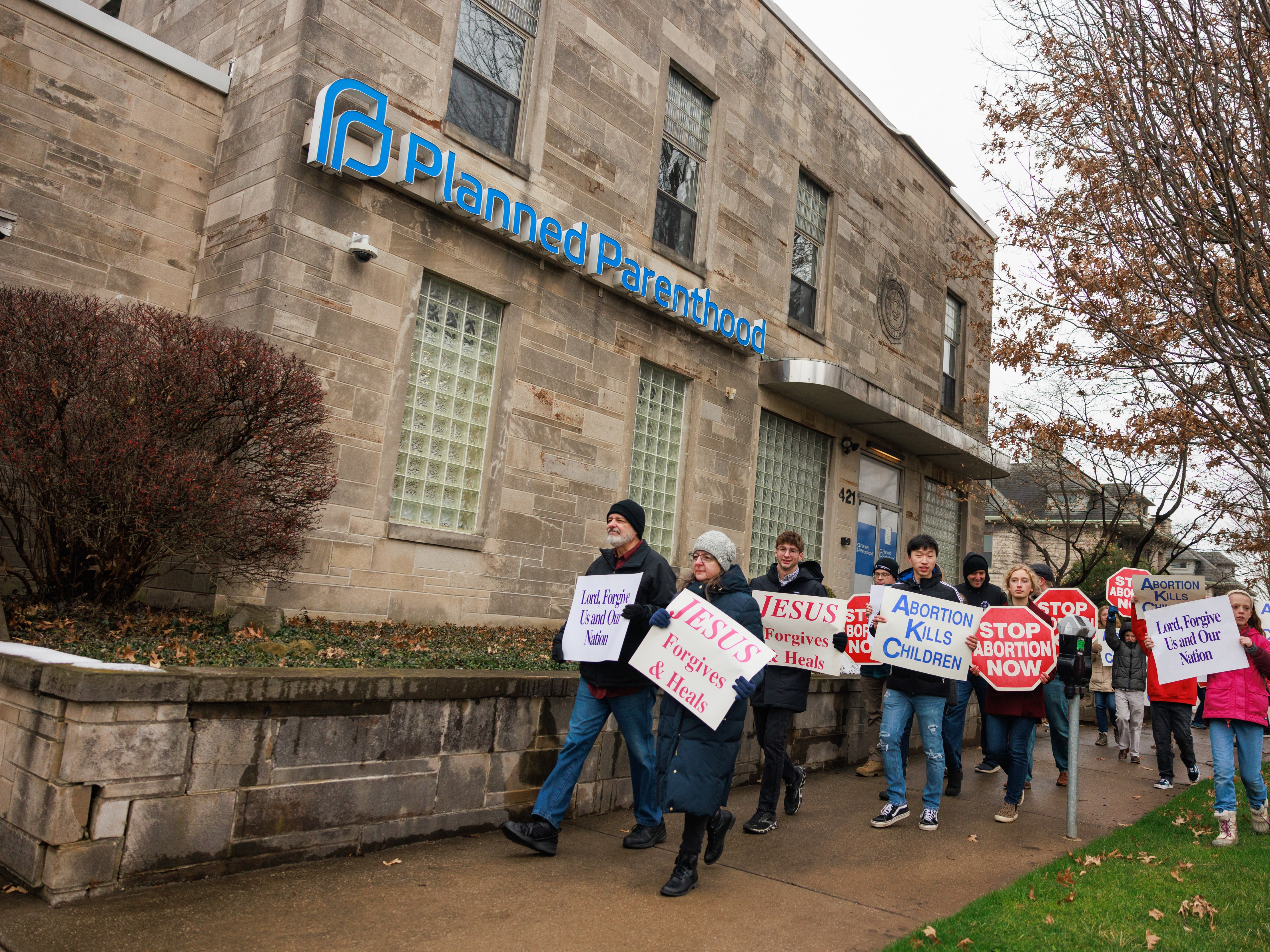 caption: Anti-abortion protesters march past the Planned Parenthood in Bloomington, Ind., after the Rally for Life march in January 2023. The facility offers birth control and testing for sexually transmitted diseases now that abortion is banned in Indiana.