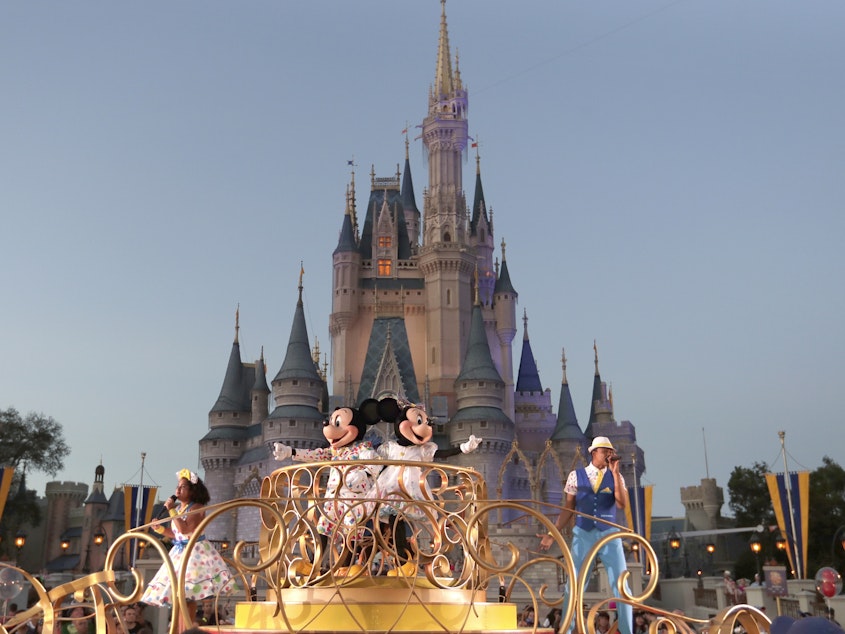 caption: Mickey and Minnie Mouse perform during a parade as they pass by the Cinderella Castle at the Magic Kingdom theme park at Walt Disney World in Florida. The theme park resort announced Tuesday that face coverings will be optional for fully vaccinated visitors in all indoor and outdoor locations.