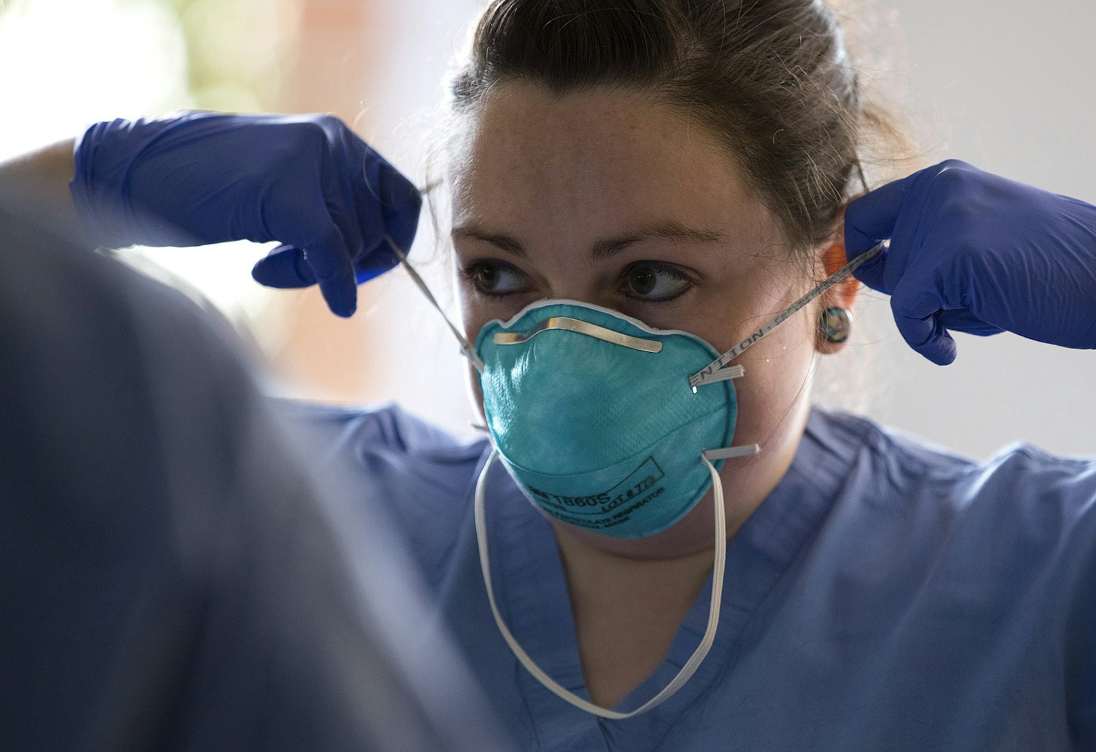 A registered nurse at UW Northwest, demonstrates to another nurse how to properly remove a mask.