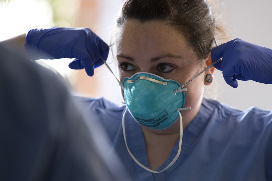 caption: Jess White, a registered nurse at UW Northwest, demonstrates to another nurse how to properly remove a mask on Thursday, March 12, 2020, at UW Medicine's drive-through testing clinic in Seattle. 