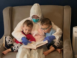caption: Dr. Lauren Jenkins reads to her twin sons, Pierce and Ashton, while wearing her "hazmat" suit. Because lung cancer has compromised her husband's immune system, Jenkins moved out of her home and visited in the suit as a precaution.