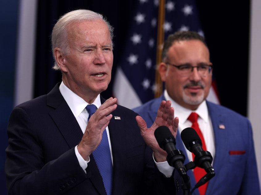 caption: President Joe Biden speaks on the student debt relief plan as Secretary of Education Miguel Cardona listens in the Eisenhower Executive Office Building on Oct. 17, 2022, in Washington, D.C.