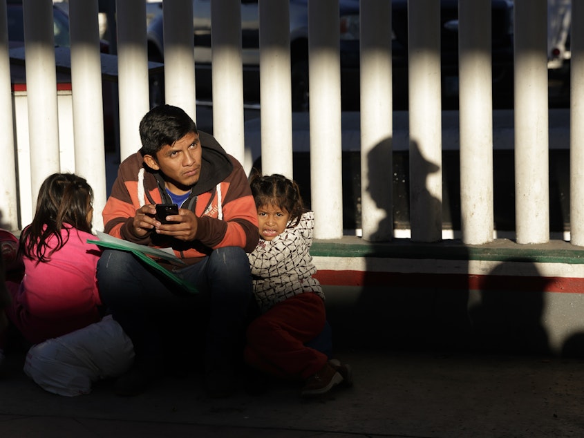 caption: A migrant and his children wait to hear if their number is called to apply for asylum in the United States, at the border in Tijuana, Mexico.