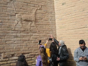 caption: Visitors with the Bil Weekend tourism company take photographs inside the ruins of the ancient city of Babylon, in the area around the Ishtar gate. The animal on the walls ins a dragon-like creature associated with the Babylonian god Marduk.