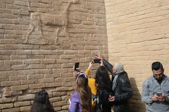 caption: Visitors with the Bil Weekend tourism company take photographs inside the ruins of the ancient city of Babylon, in the area around the Ishtar gate. The animal on the walls ins a dragon-like creature associated with the Babylonian god Marduk.