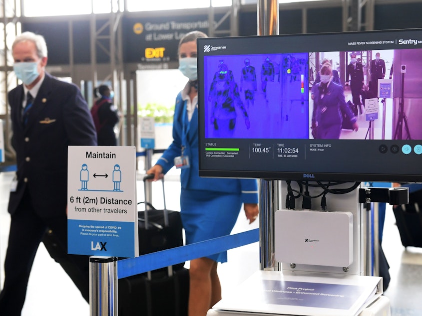 caption: Flight crew walk past thermal cameras that check passengers' body temperatures at Los Angeles International Airport on June 23. As businesses look to reopen, technology firms are offering an array of monitoring systems to try to control the coronavirus.