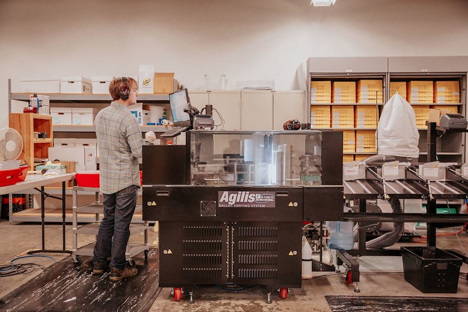 caption: A large sorting machine is the first stop for ballots at the Pierce County Election Center, before workers verify they each contain a valid signature and continue processing them.