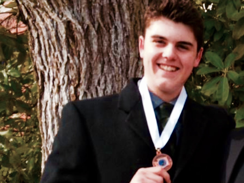 caption: Calvin Clark in his senior year of high school, holding up a medal for the state debate championship.