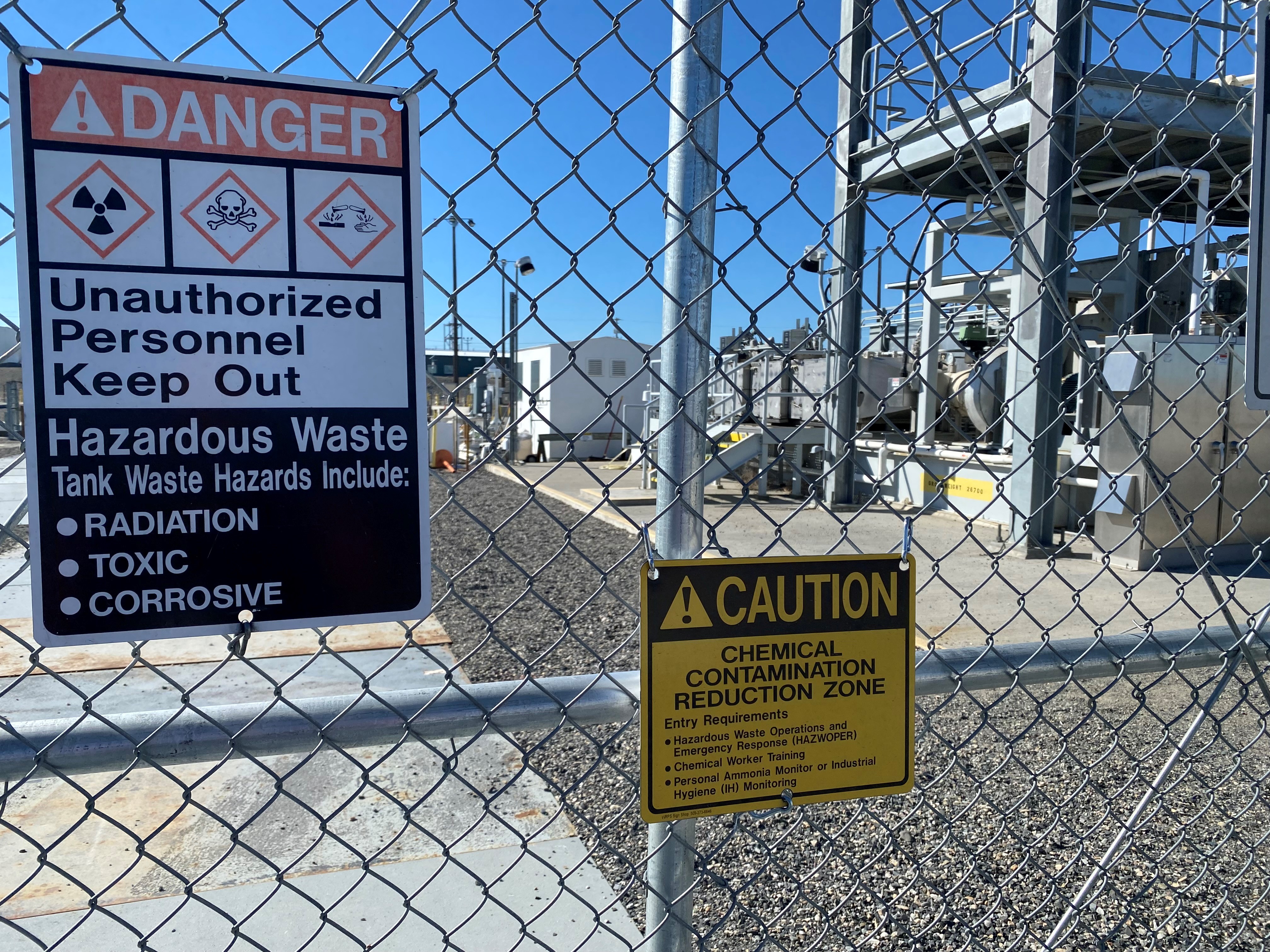 caption: A gate and signs stand guard at one of the Hanford site’s tank farms.