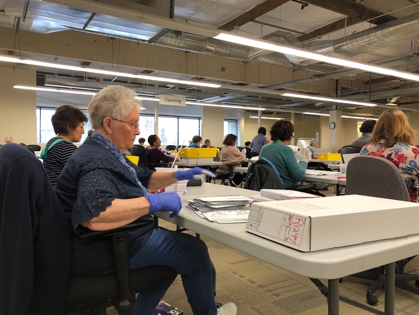 caption: King County Elections has hired up to 150 temporary staff to process ballots. Jane Reese, left, says they're taking precautions to prevent virus transmission.