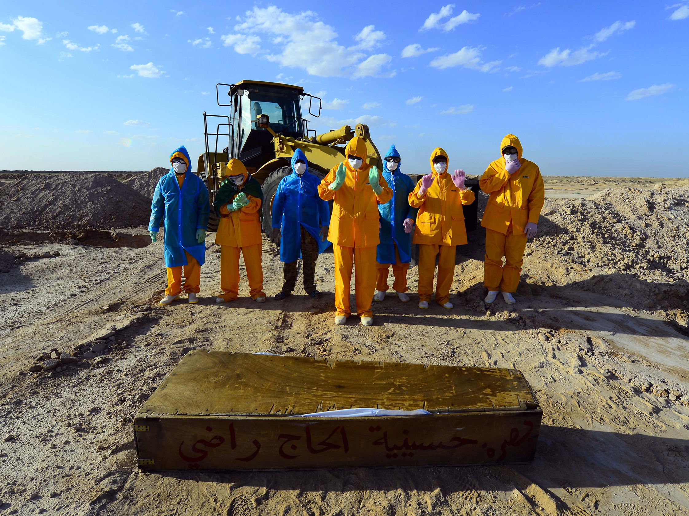 caption: On April 3, Iraqi volunteers in full hazmat gear prayed over the coffin of a 50-year-old who died of COVID-19. She was buried at a cemetery specifically opened for such deaths, some 12 miles from the holy city of Najaf.