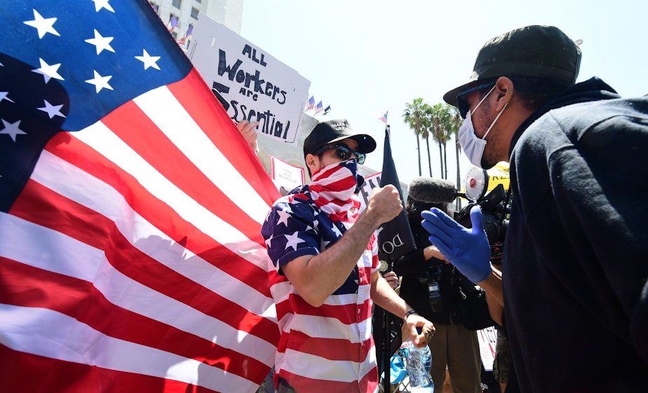 caption: A protestor (L) argues with a counter-protestor (R) in front of the Los Angeles City Hall on May 1, 2020, to demand the end to the state's shutdown due to the coronavirus pandemic. (FREDERIC J. BROWN/AFP via Getty Images)