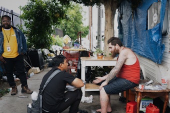 caption: Anthony Velbis, a nurse with the homeless service agency HOPICS, checks up on Anthony Boladeres outside the RV where he's living in South Los Angeles. "It's nice being able to meet the client where they're at," Velbis says.