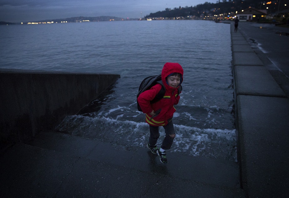 caption: Ely Thomas, 7, runs from water spilling over stairs during a King Tide at Alki Beach Park on Friday, January 5, 2018, in West Seattle. 