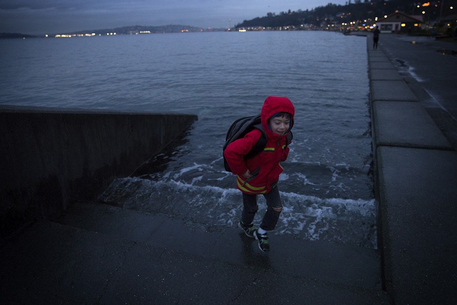 caption: Ely Thomas, 7, runs from water spilling over stairs during a King Tide at Alki Beach Park on Friday, January 5, 2018, in West Seattle. 