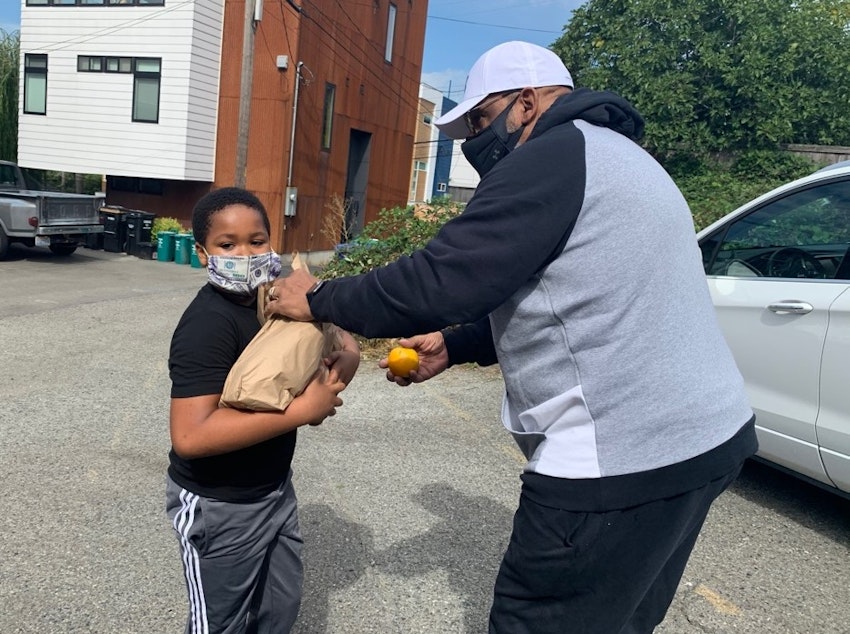 caption: Gerald  Donaldson, a family support worker at Leschi Elementary in Seattle, hands off some school lunches to third-grader Elijah Baker.