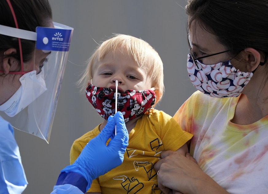 caption: One-year-old Quentin Brown, is held by his mother, Heather Brown, as he eyes a swab while being tested for COVID-19 at a new walk-up testing site at Chief Sealth High School, Friday, Aug. 28, 2020, in Seattle. The child's daycare facility requires testing for the virus. The coronavirus testing site is the fourth now open by the city and is free. 