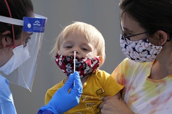 caption: One-year-old Quentin Brown, is held by his mother, Heather Brown, as he eyes a swab while being tested for COVID-19 at a new walk-up testing site at Chief Sealth High School, Friday, Aug. 28, 2020, in Seattle. The child's daycare facility requires testing for the virus. The coronavirus testing site is the fourth now open by the city and is free. 