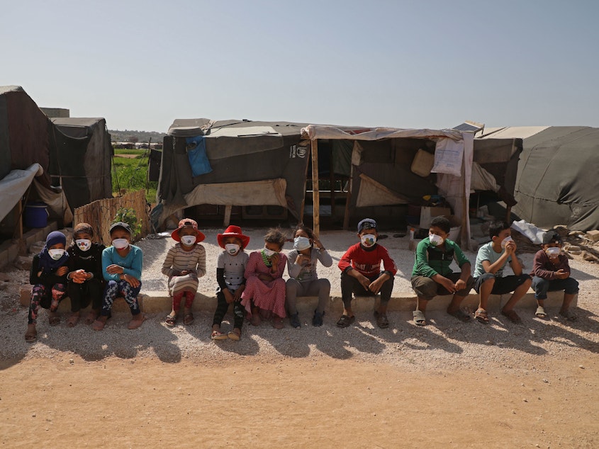 caption: Children displaced by the war in Syria's Idlib province sit, wearing face masks during a COVID-19 awareness campaign this week in Dana. The World Food Programme warned that people living in displaced-person camps could be "particularly vulnerable" to the pandemic's physical and economic effects.