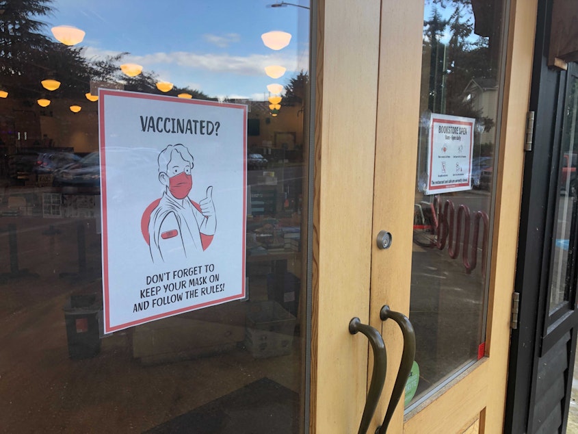 caption: A sign asking customers to keep their masks on, even if they have been vaccinated, at the front door of Third Place Books in Seattle's Seward Park neighborhood. 