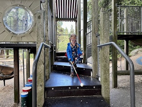 caption: Gavin Glaves navigates a play structure at Seward Park playground with a cane, July 17, 2023.