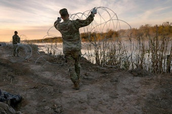 caption: Texas National Guard soldiers install additional razor wire lie along the Rio Grande on Jan. 10 in Eagle Pass, Texas.