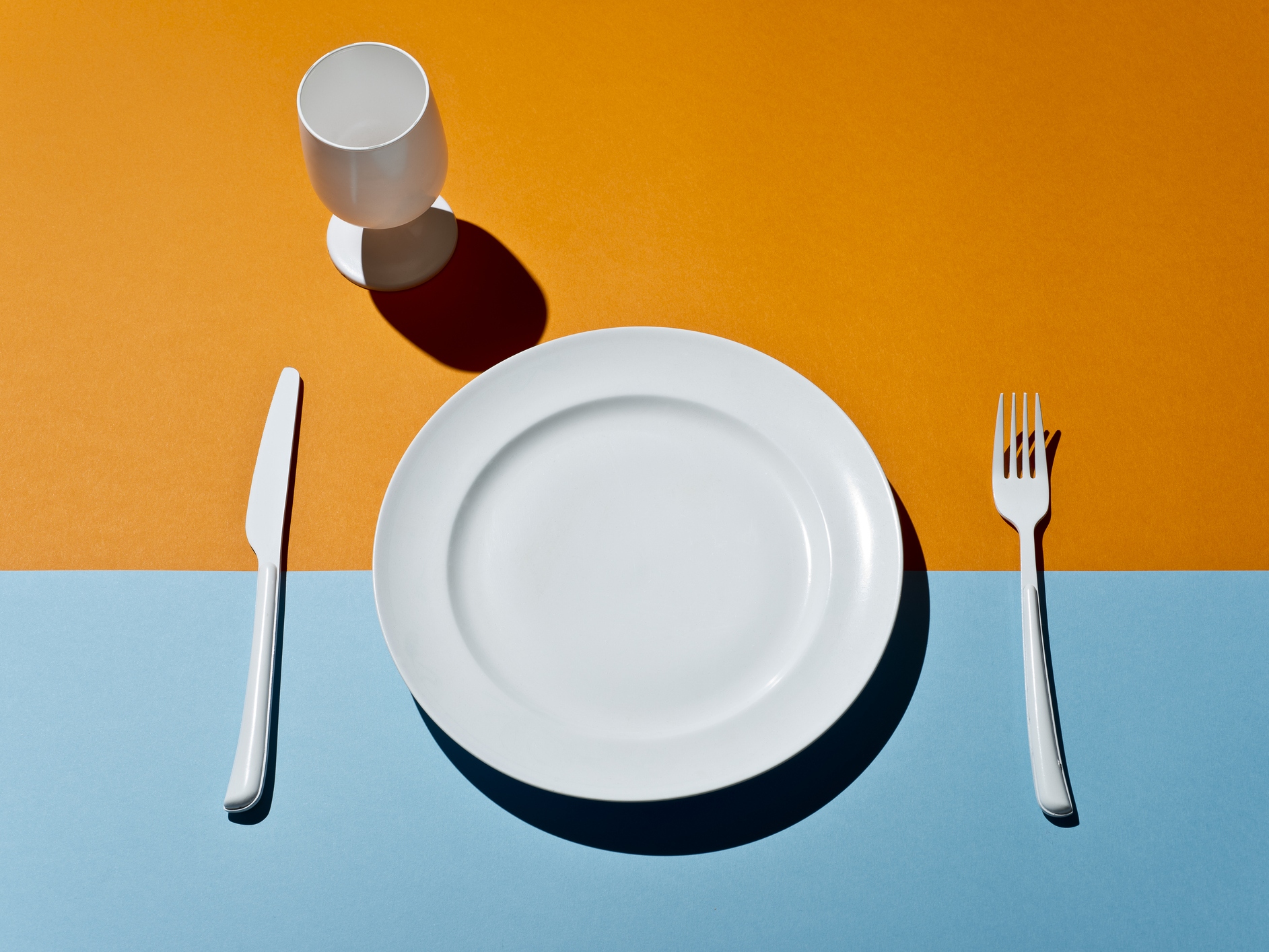 caption: High Angle View Of white glass, fork, knife and plate on a colored table