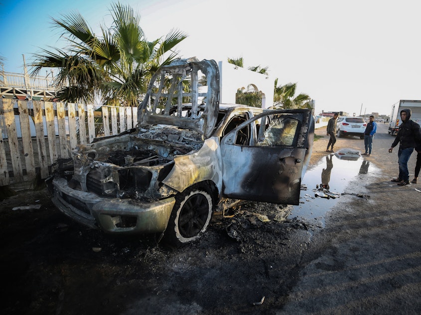 caption: People stand next to a vehicle in Deir Al-Balah, in the central Gaza Strip, on April 2, where workers from the World Central Kitchen (WCK), were killed in Israeli airstrikes, according to the NGO.