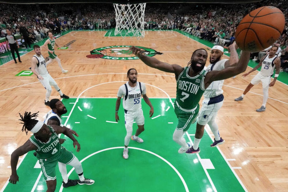 caption: Boston Celtics guard Jaylen Brown (7) drives toward the basket in front of Dallas Mavericks forward Derrick Jones Jr. (55) as Celtics guard Jrue Holiday (4) looks on during the first half of Game 5 of the NBA basketball finals in Boston. (Peter Casey/Pool Photo via AP)