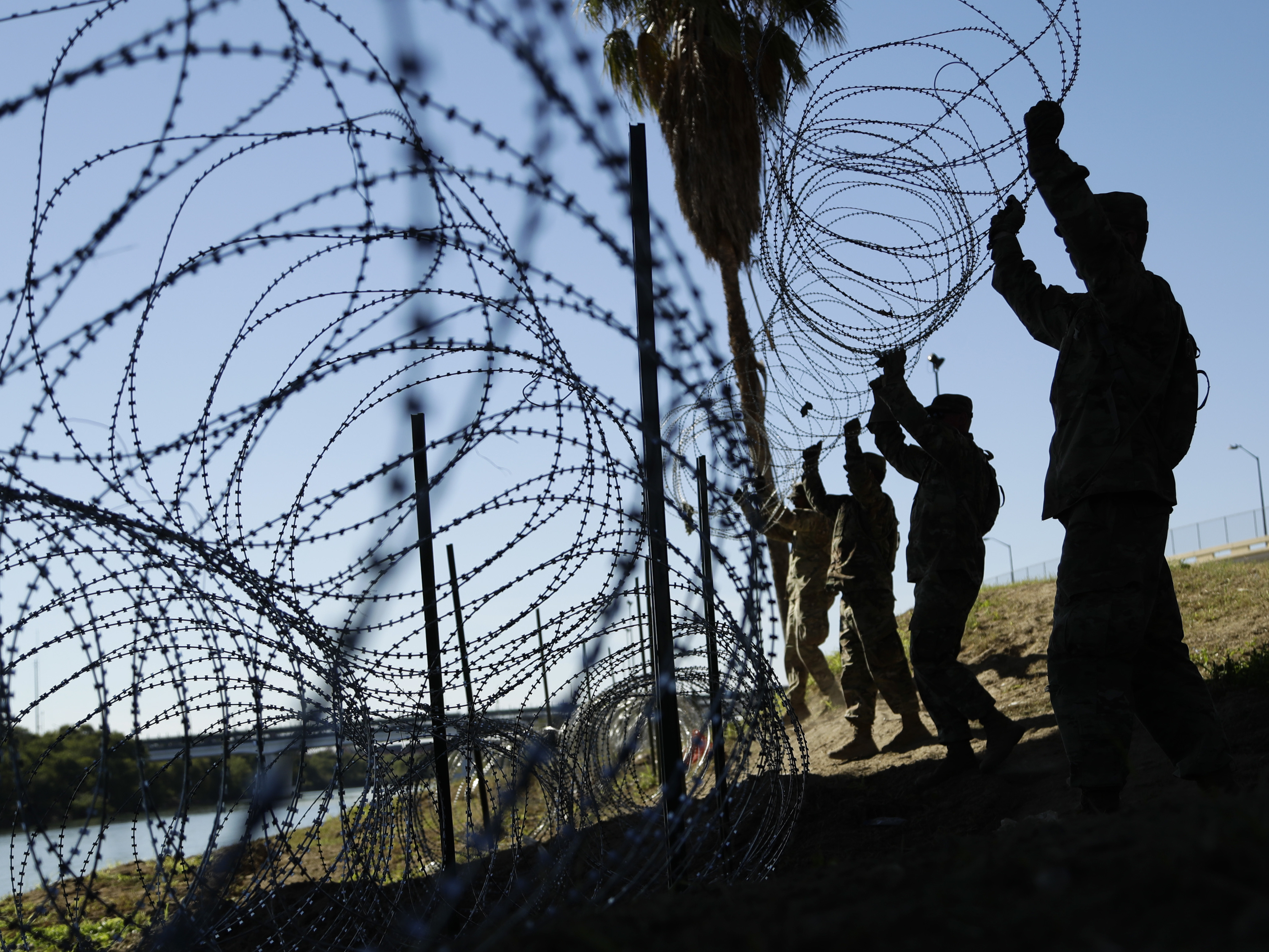 caption: Members of the U.S. military install multiple tiers of concertina wire along the banks of the Rio Grande near the Juarez-Lincoln Bridge at the U.S.-Mexico border in Laredo, Texas in November.
