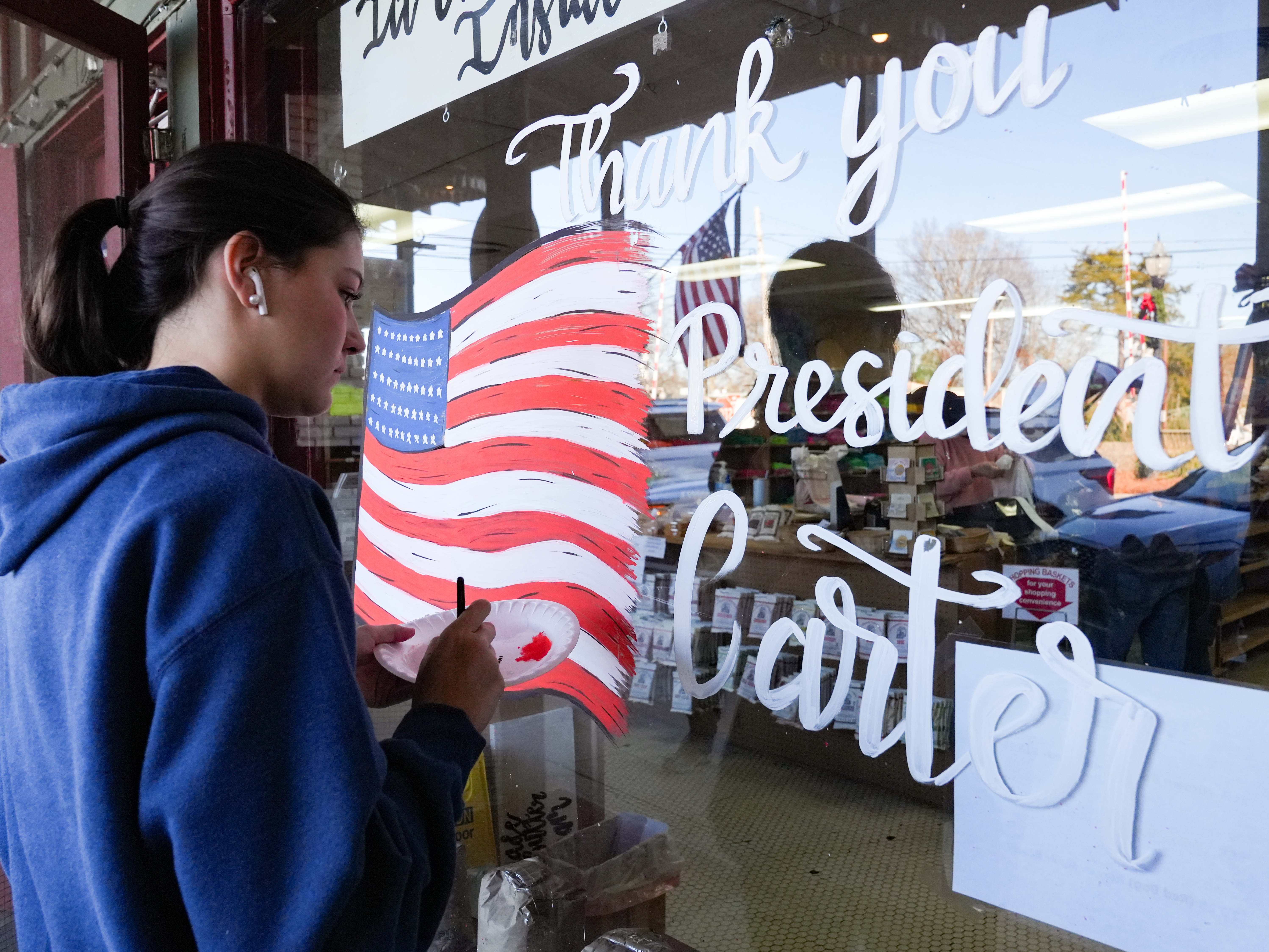 caption: Morgan Minick paints a sign thanking former President Jimmy Carter in his hometown after he died Sunday in Plains, Ga. President Carter lived to be 100 years old, making him the longest living U.S. president in history.