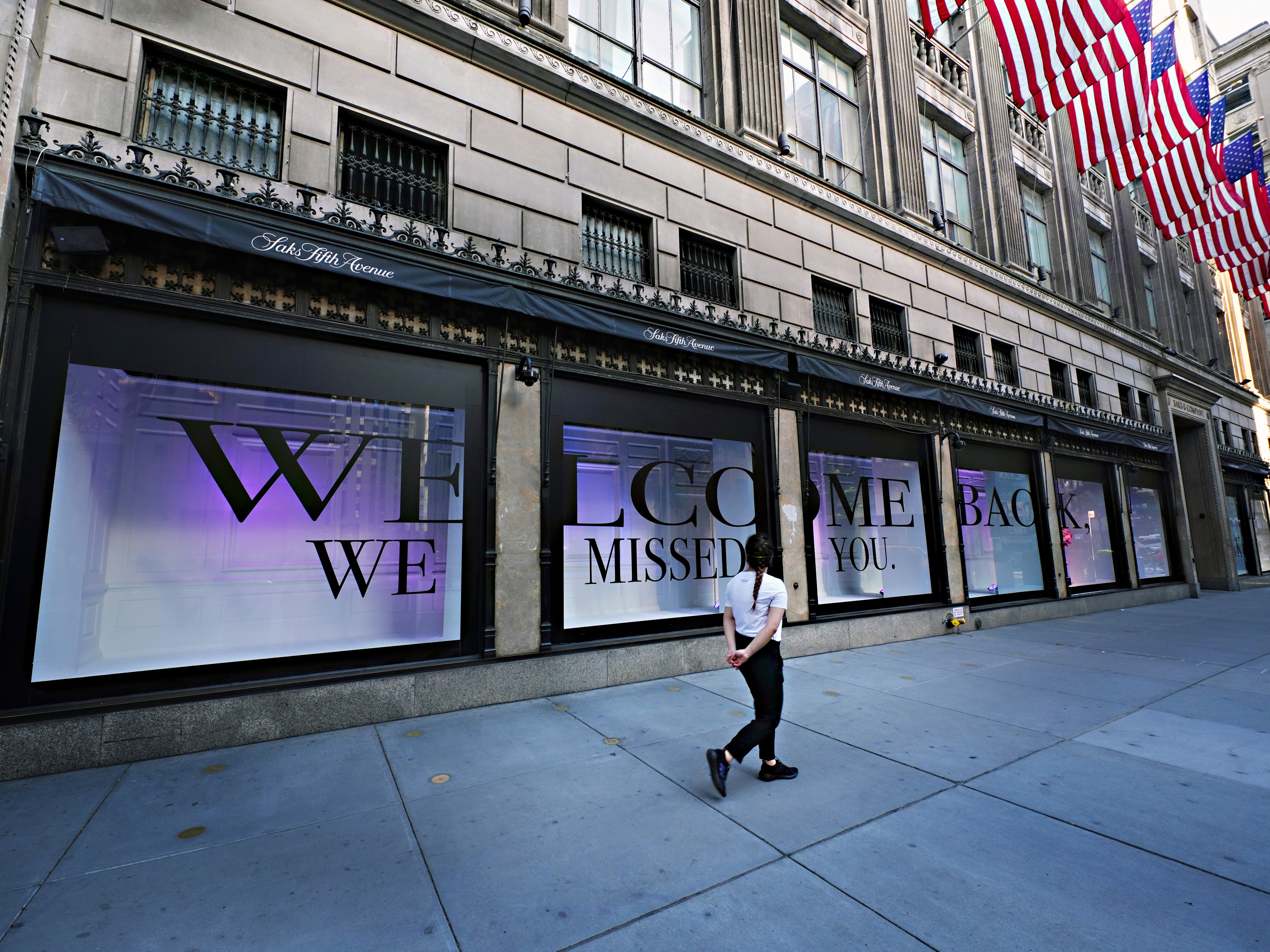 caption: A pedestrian walks by Saks Fifth Avenue as New York City continues relaxing more restrictions imposed to curb the coronavirus pandemic.