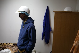 caption: Abdirahman Shire in his dormitory room. Room and board are free or cost less than $15 a day for seafood processing workers (depending on their contract and from plant to plant). 