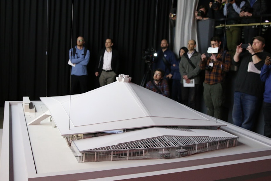 caption: Reporters watch a promotional video with a model of the new Seattle Center Arena in the foreground