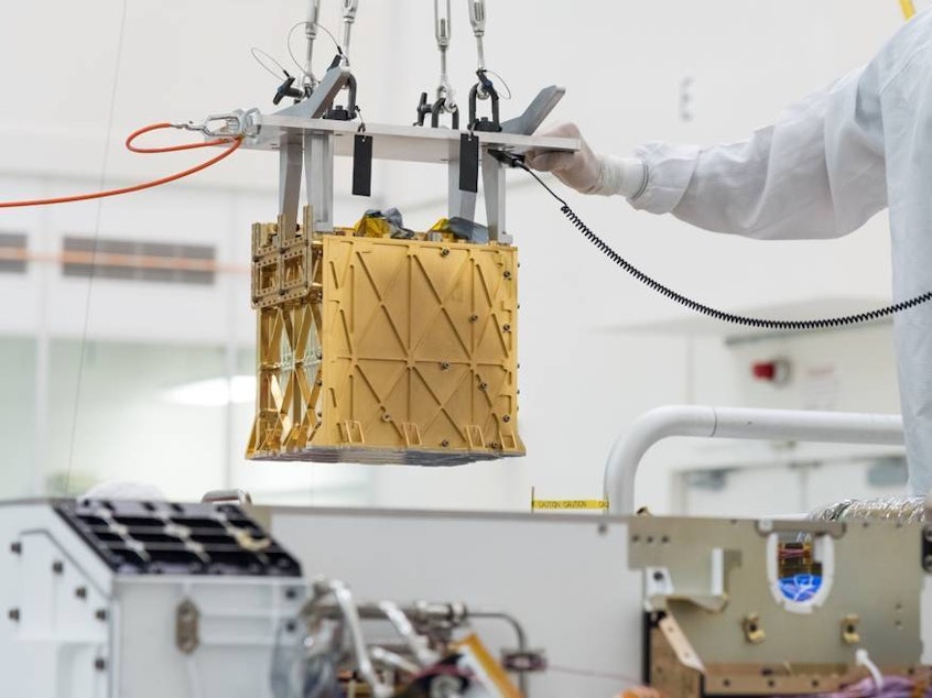 caption: Technicians at NASA's Jet Propulsion Laboratory lower the Mars Oxygen In-Situ Resource Utilization Experiment (MOXIE) instrument into the belly of the Perseverance rover. NASA announced that the instrument had produced oxygen from the Martian atmosphere.