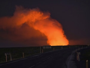 caption: A view of the plume of gas lighted up by the lava from the erupting volcano seen from Suðurstrandavegur, the road that leads to Grindavík, Iceland, on Sunday.